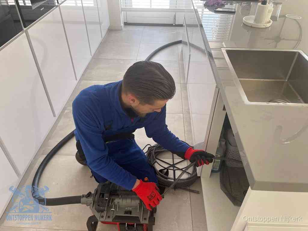Een monteur ontstopt de keukenafvoer onder de spoelbak met een elektrische veermachine in Nijkerk