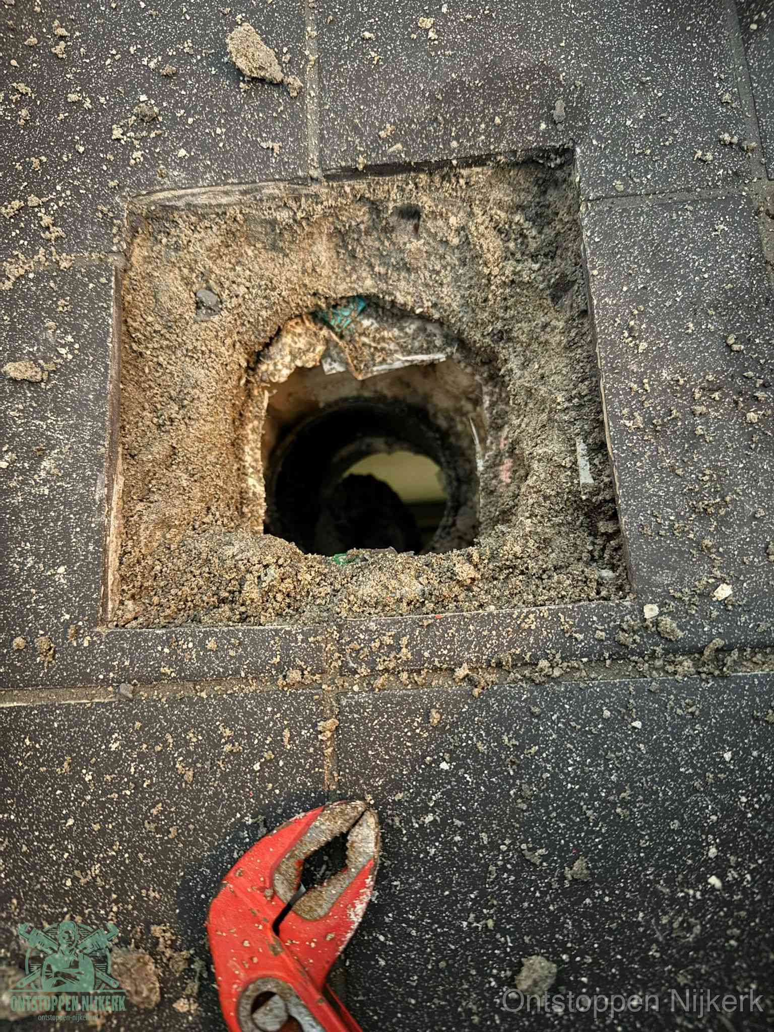 Een geopend rioolputje in een betontegelvloer met losgemaakt rooster en een zichtbare ronde afvoerbuis, het achterhalen waar de afvoerverstopping zit in Nijkerk