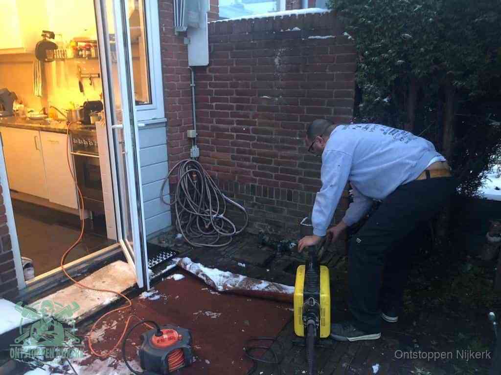 Een monteur werkt buiten bij een open riool-/grondput met een elektrische ontstoppingsmachine om een verborgen afvoerprobleem op te sporen in Nijkerk