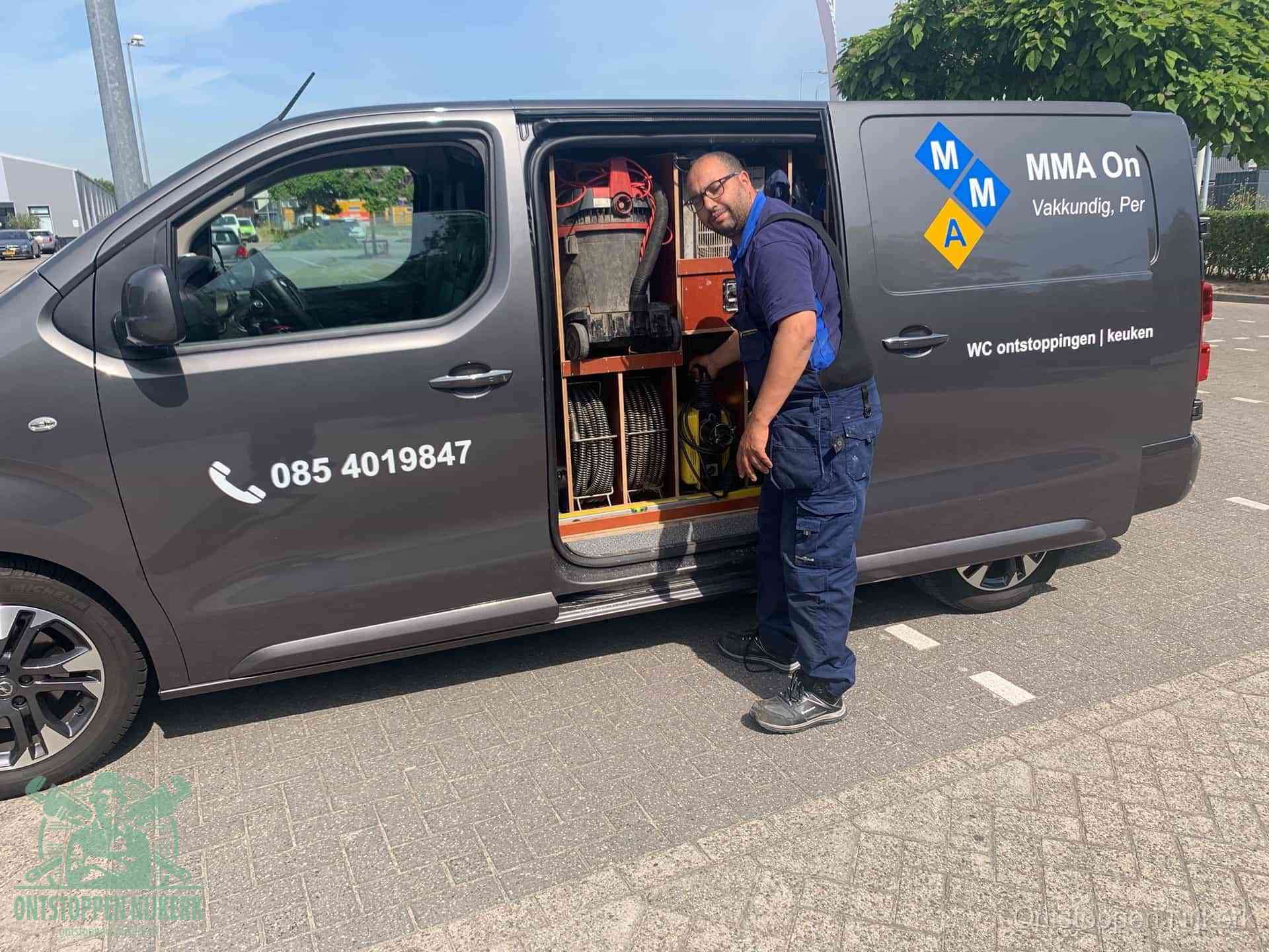 Een monteur bij de open schuifdeur van zijn bedrijfsbus op een parkeerplaats, klaar om de oorzaak van terugkerende afvoerverstoppingen aan te pakken in Nijkerk