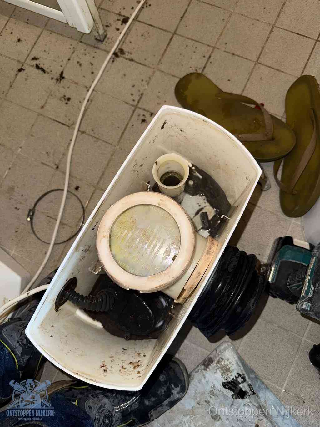 Een gedemonteerde toiletpot op de vloer met ontstoppingsveer en gereedschap ernaast, het verwijderen van een vastzittend voorwerp uit de wc in Nijkerk