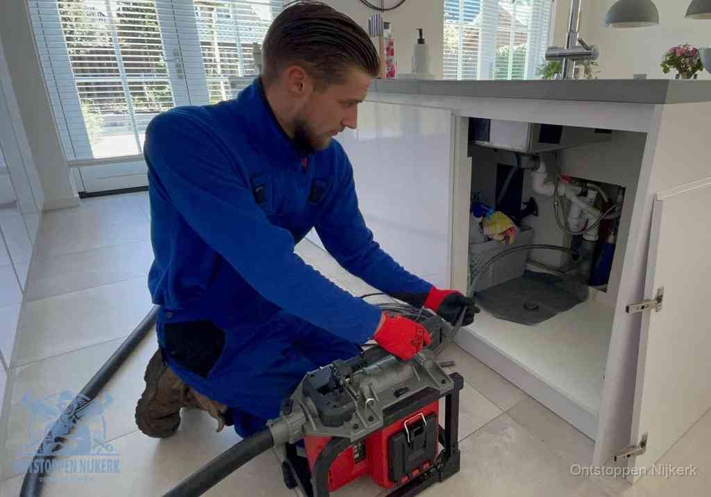 Een monteur voert een professionele elektrische ontstoppingsmachine in de afvoer onder de spoelbak tijdens het gootsteen ontstoppen in Nijkerk